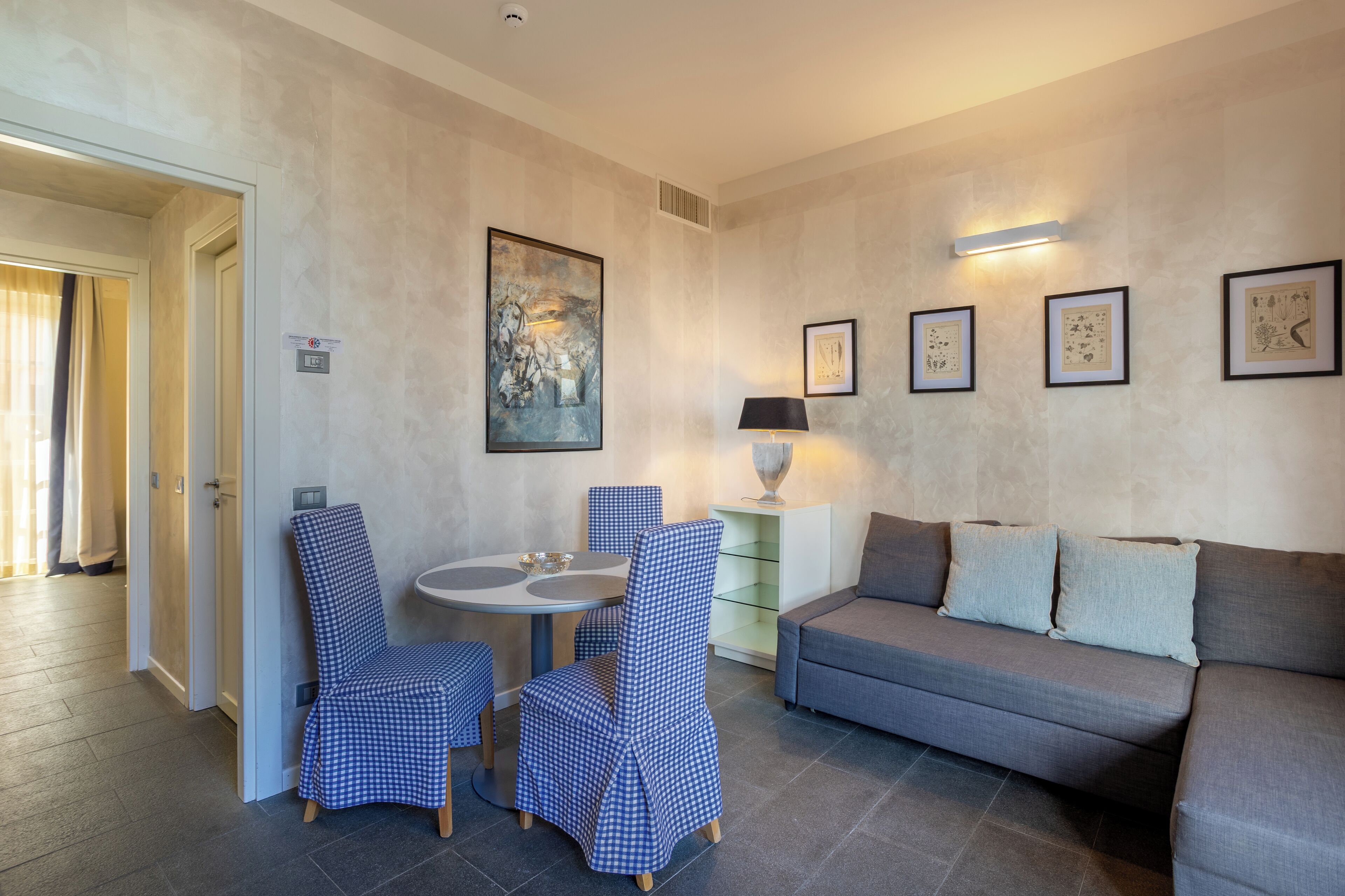 A modern living room with a grey sofa, blue checkered chairs, a round table, and a wall-mounted lamp.