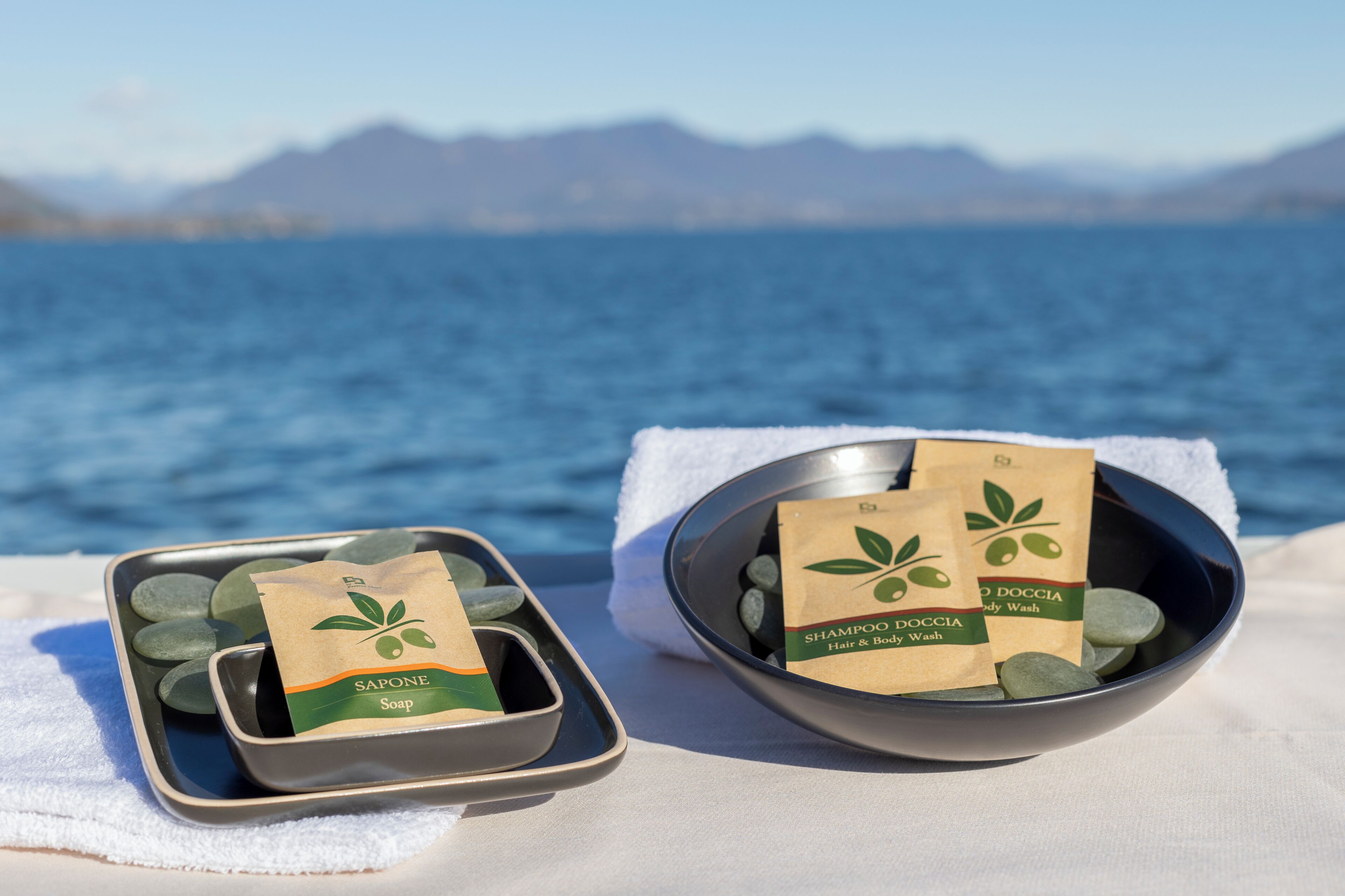 A spa setting with a bowl of soap and shampoo bags on a towel by a body of water.