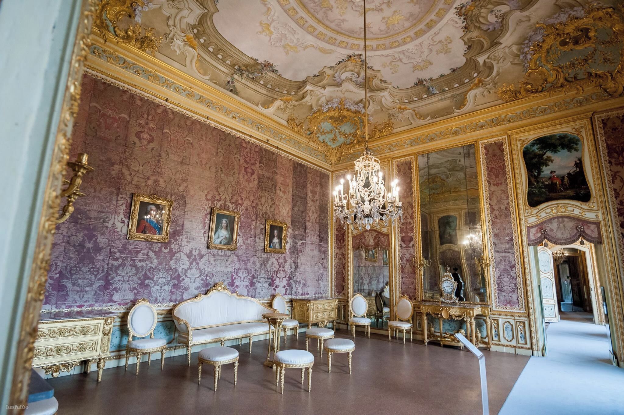 An opulent room with ornate gold detailing, a grand chandelier, and classical paintings.