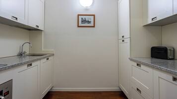 Una cucina compatta con mobili bianchi, un piano di lavoro in granito, forno integrato e una singola foto incorniciata appesa al muro.