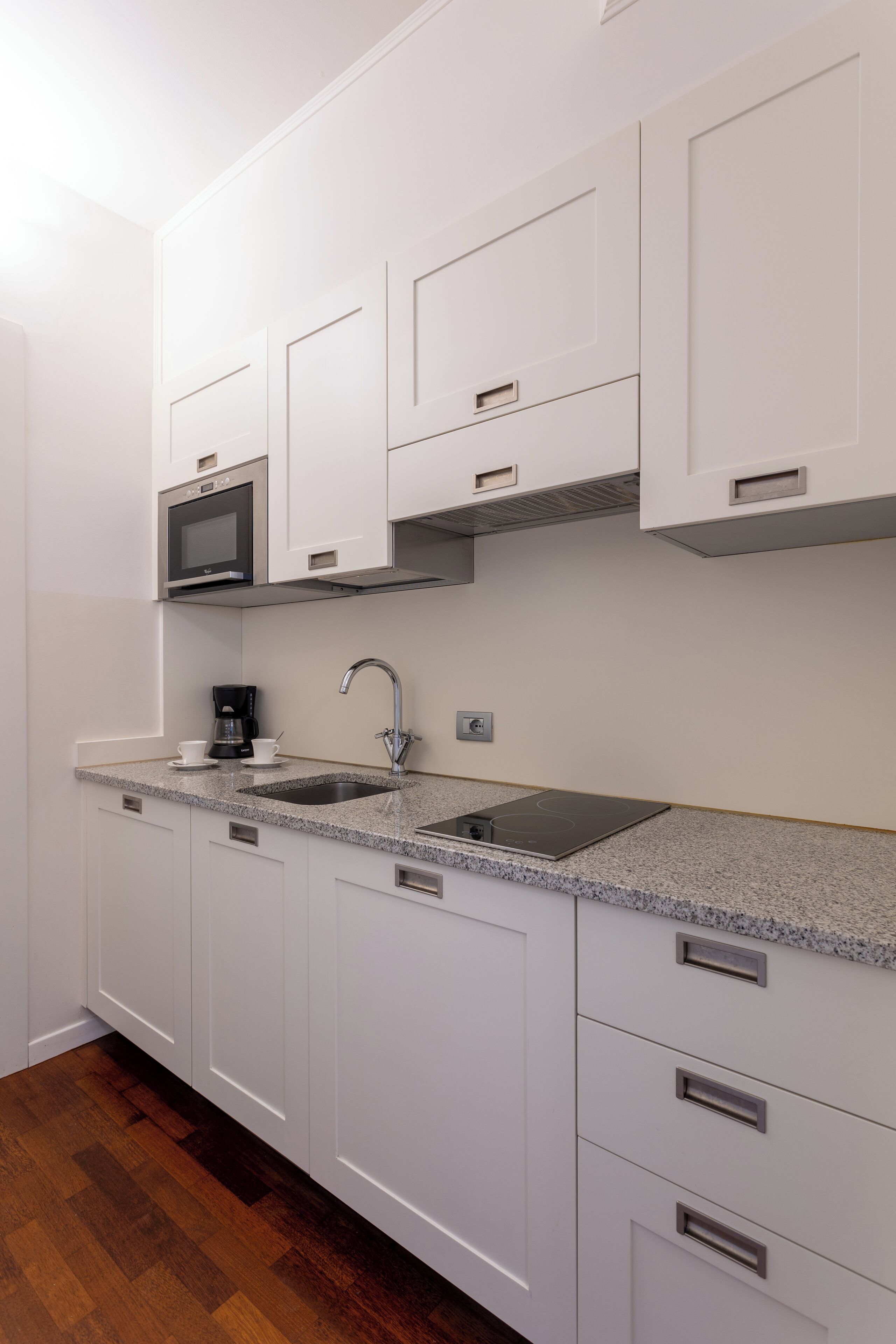 A modern kitchen with white cabinets, a granite countertop, a built-in microwave, a coffee maker, and a stainless steel sink.