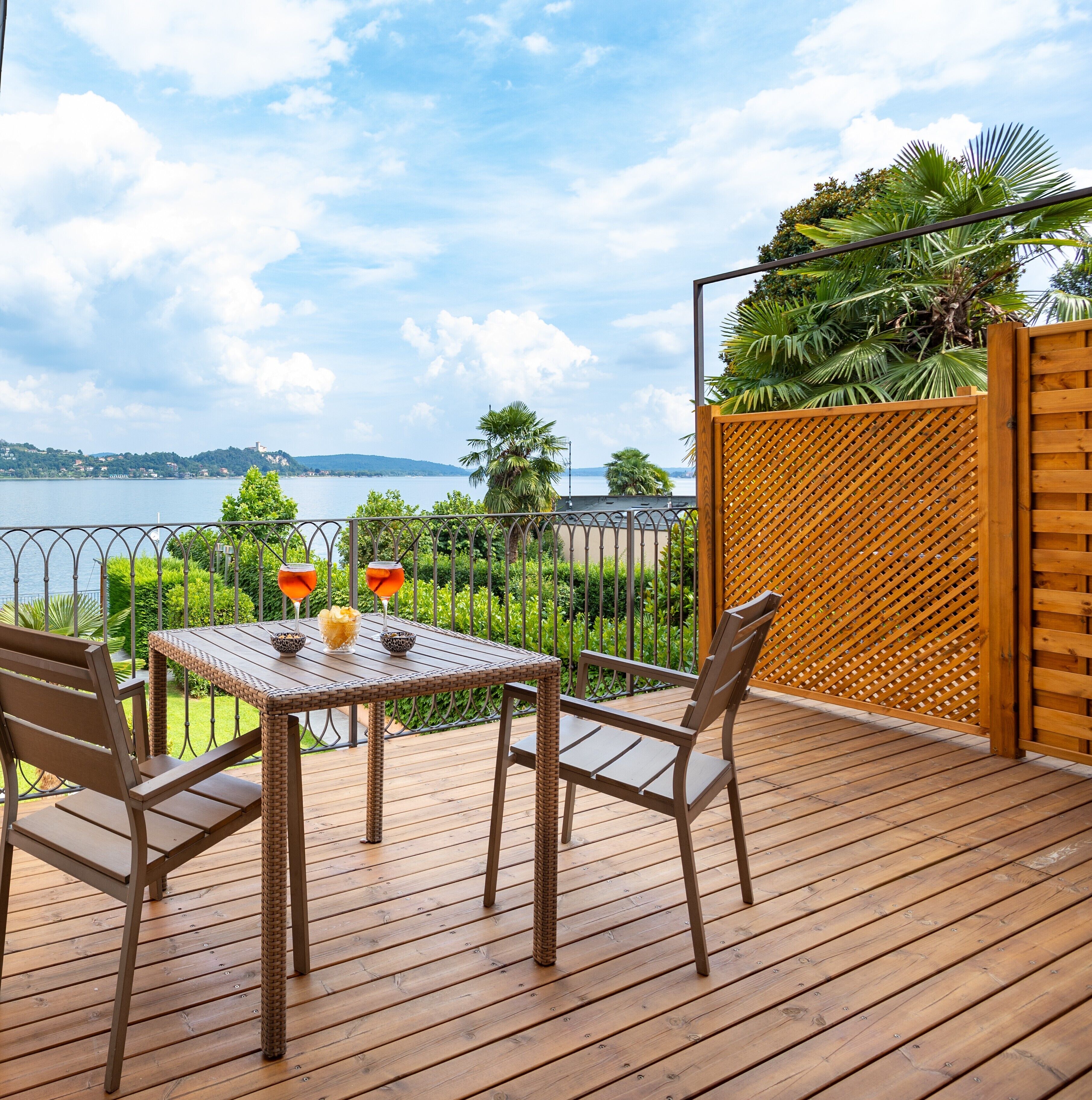 Terraza de madera con una mesa y sillas, con vista a un lago y colinas distantes, además de una masa de agua.