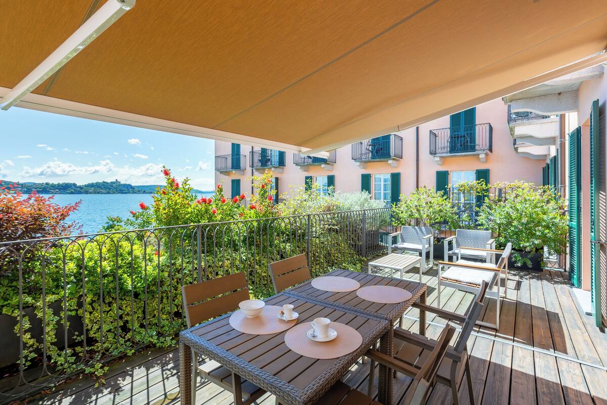 Une terrasse en bois avec une table dressée pour deux personnes, entourée de verdure et offrant une vue sur l’eau.