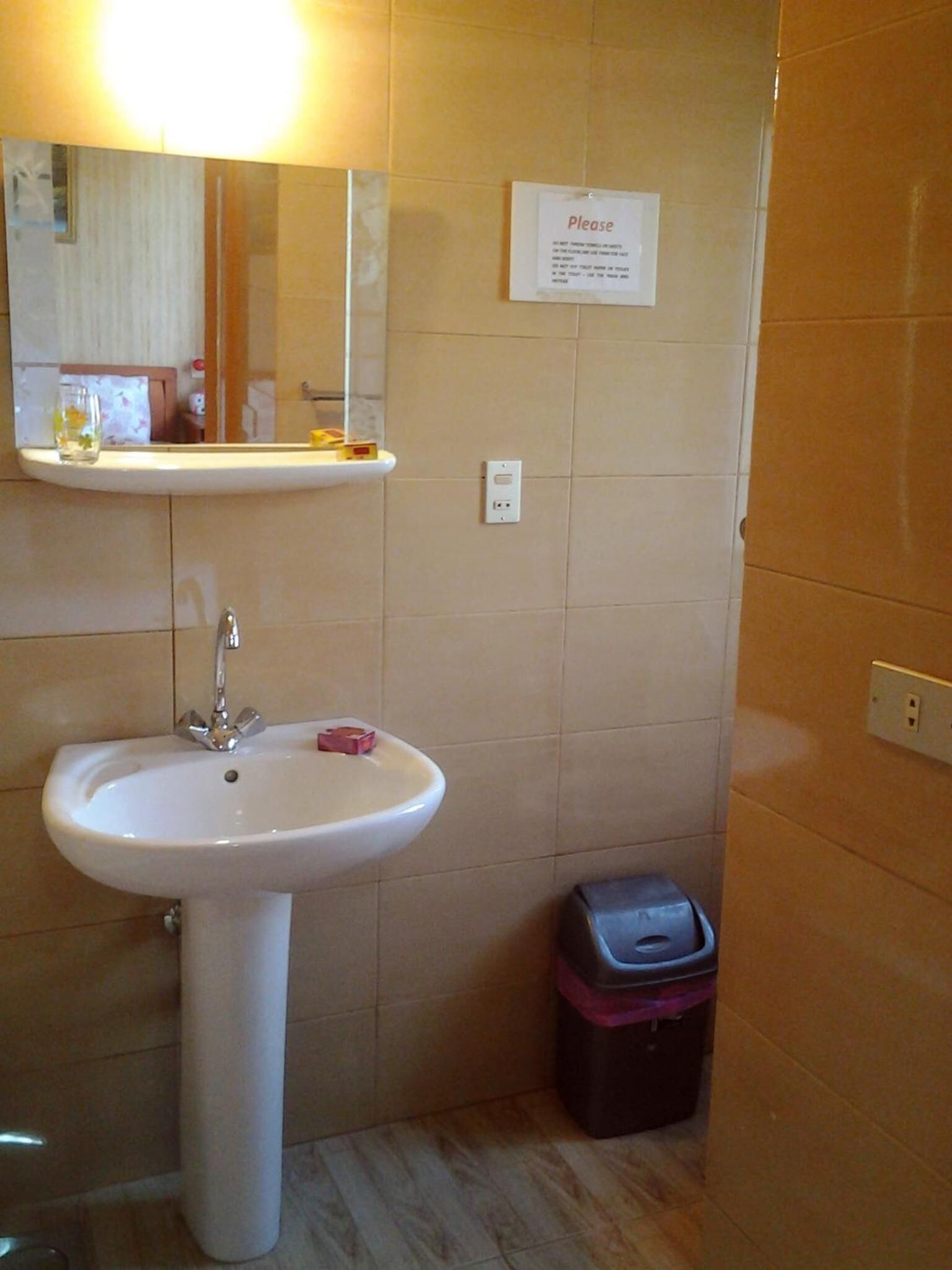 A bathroom with a white sink, a mirror, a trash bin, and a sign on the wall.