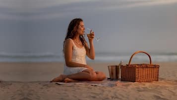 Una persona sentada sobre una toalla de playa con una cesta de picnic a su lado.