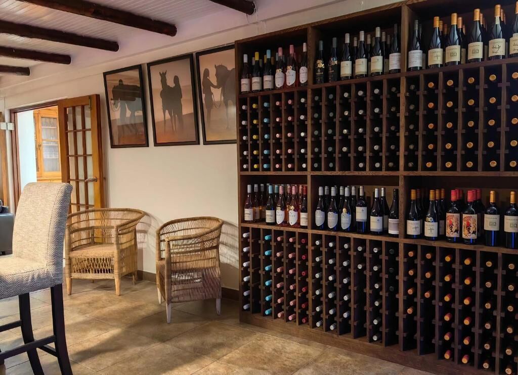 Una cava de vinos con varias estanterías, sillas de mimbre y obras de arte enmarcadas en la pared.