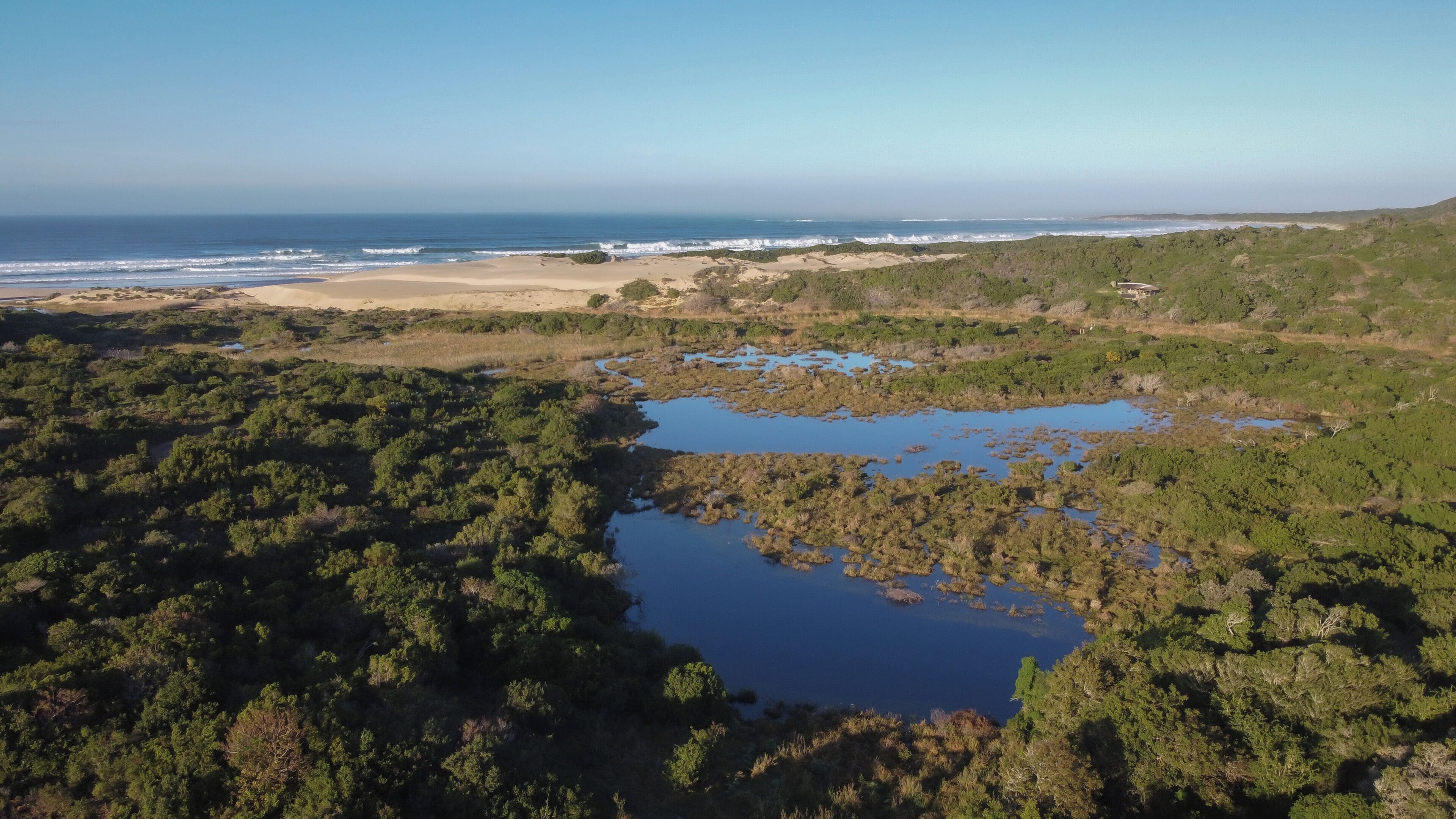 Vista aérea de una zona costera con playa, dunas y humedales con cuerpos de agua.