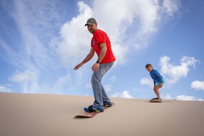 Un homme et un enfant font de la planche à neige sur une dune de sable.