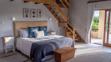 Un dormitorio con una escalera de madera, una cama con almohadones estampados, una mesita de noche y vistas al verde a través de la ventana.