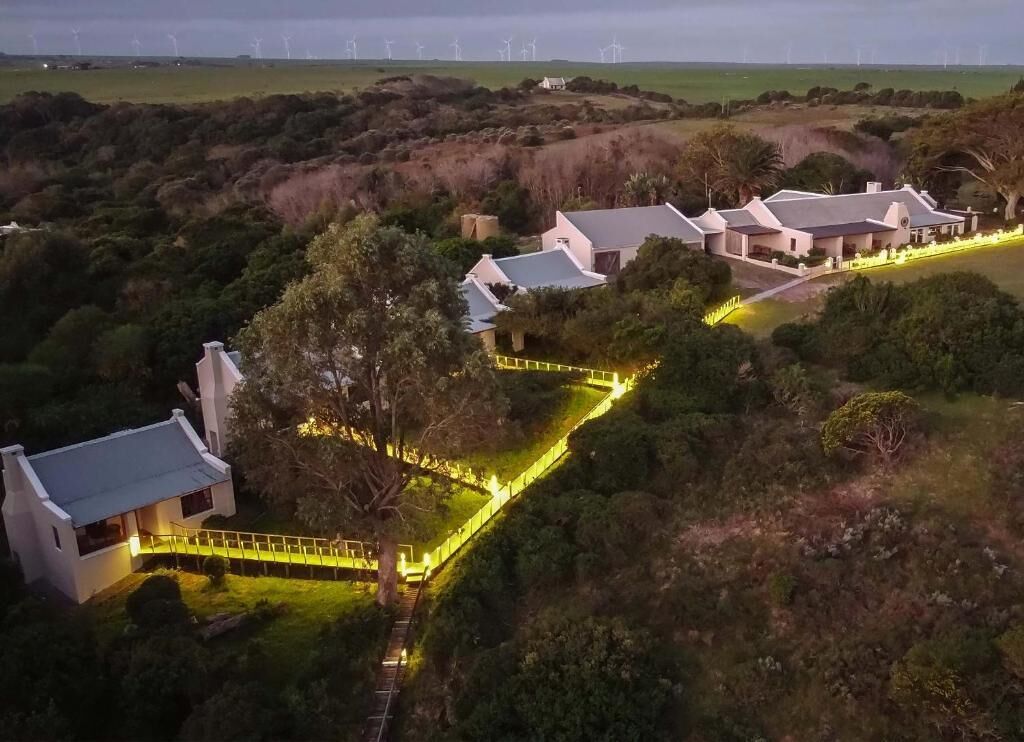 Un barrio residencial con varias casas, un sendero sinuoso y aerogeneradores a lo lejos.