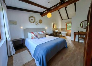 Un dormitorio con una cama grande, techo de madera y un baño visible al fondo.