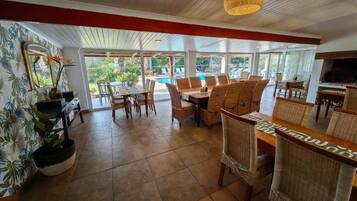 Amplio espacio interior con mesa y sillas, un espejo grande y vistas a una piscina exterior.