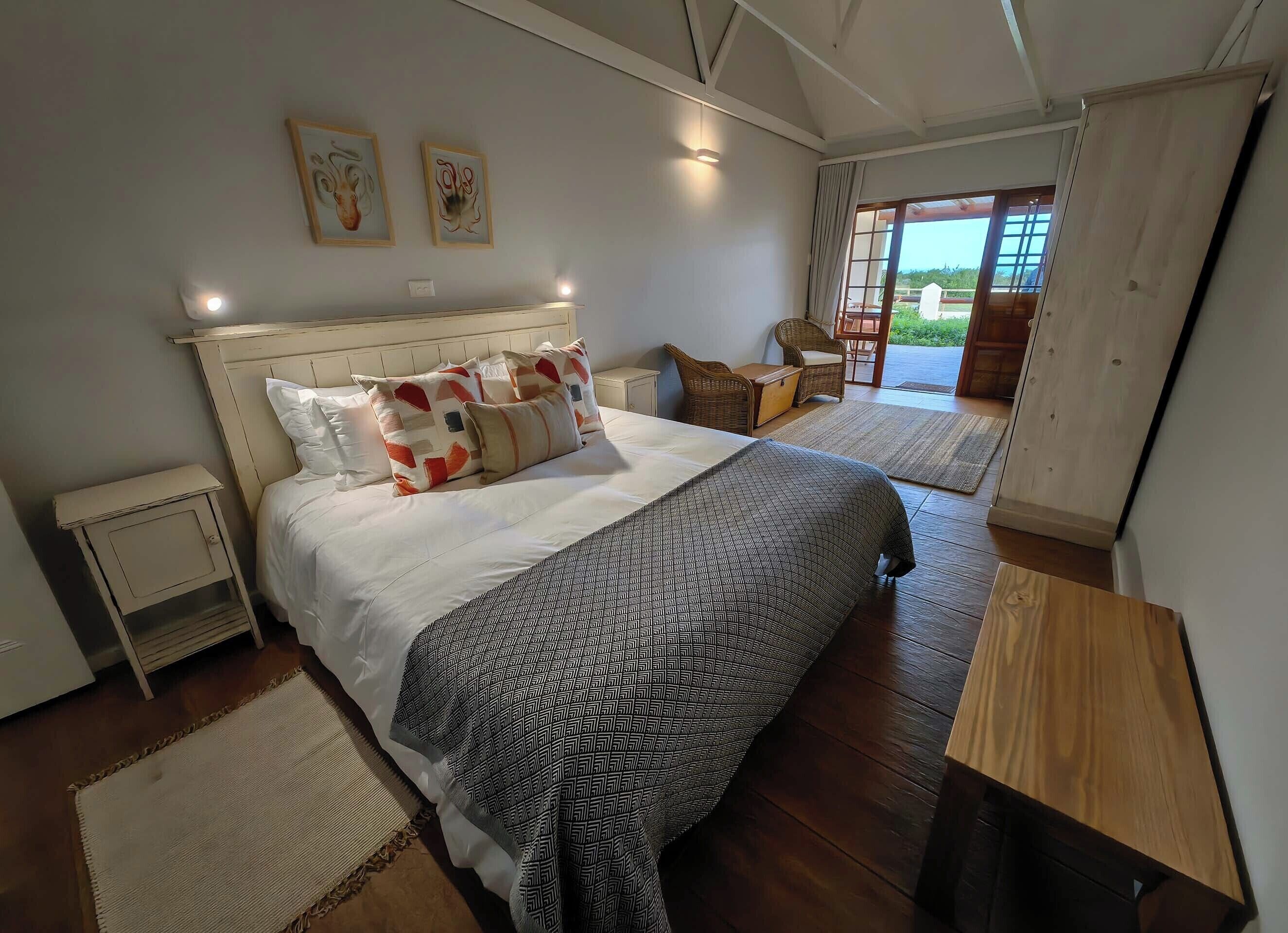 Ein Schlafzimmer mit einem großen Bett, einem Nachttisch, einem Sessel und Blick ins Freie.
