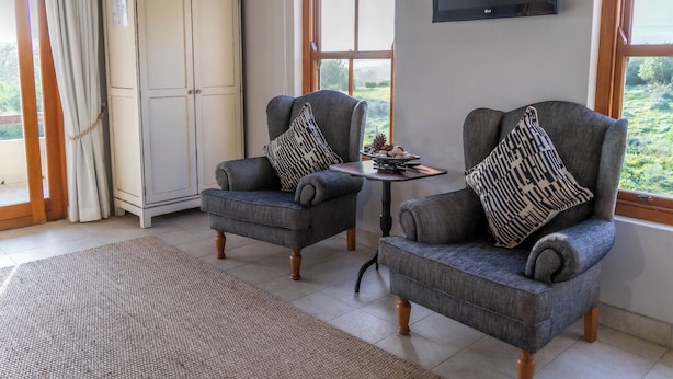 A room with two grey armchairs, a small table with a decorative bowl, a white cabinet, and a TV mounted on the wall.