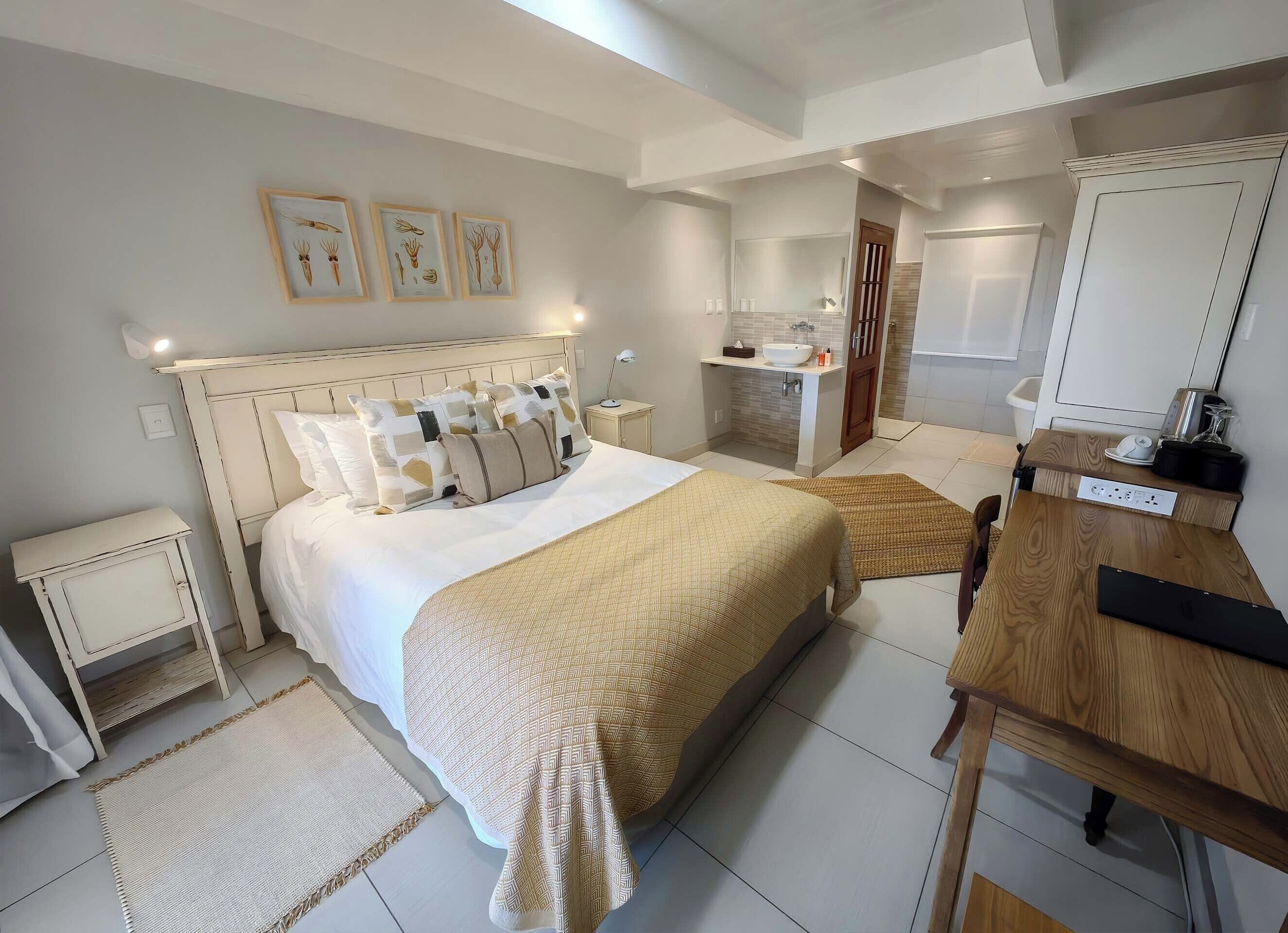 A bedroom with a large bed, bedside tables, a wooden desk, and a bathroom with a sink and mirror.