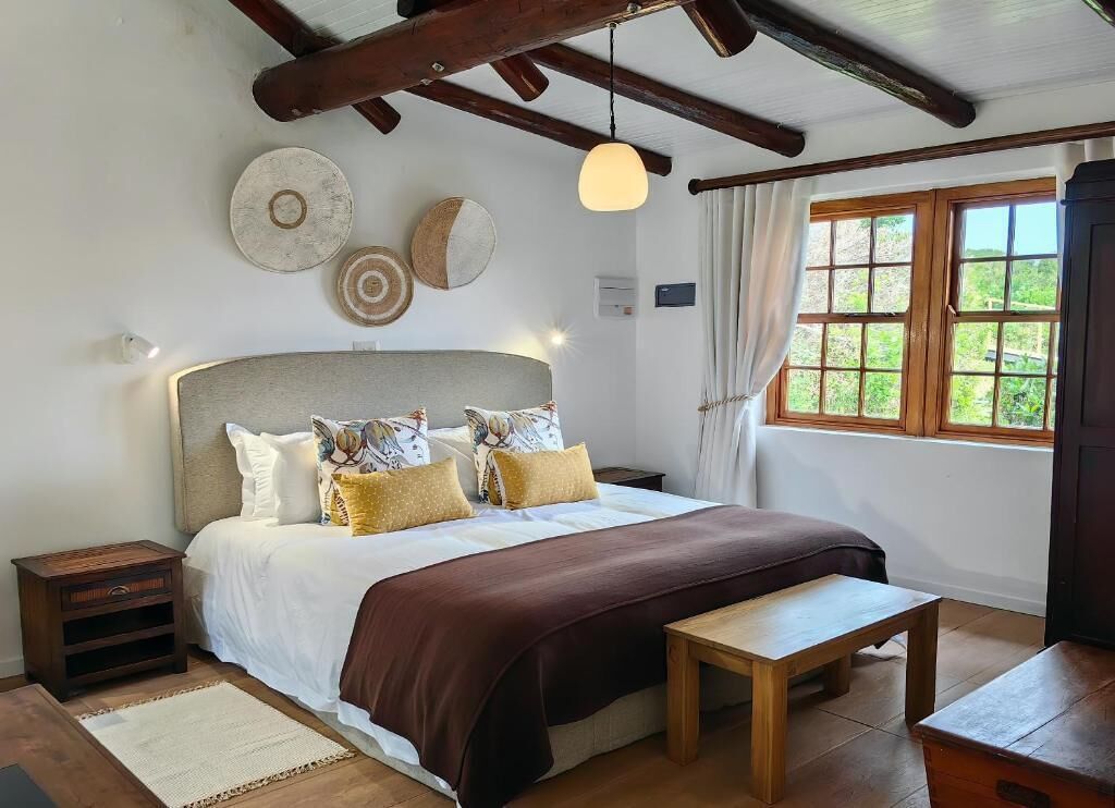 Un dormitorio con una cama grande, cabecera de madera, mesitas de noche, un banco y una ventana con cortinas.