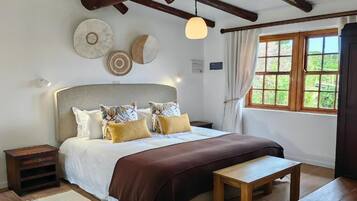 Un dormitorio con una cama grande, cabecera de madera, mesitas de noche, un banco y una ventana con cortinas.