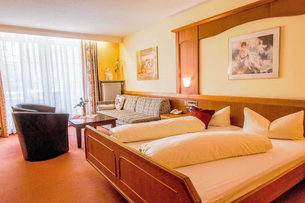 A hotel room with a large bed, a sofa, a desk, and a chair.