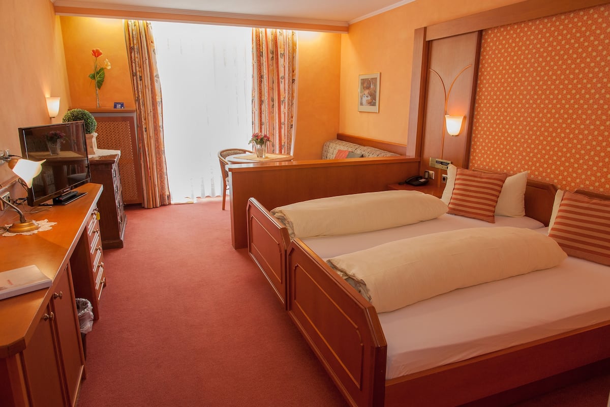 A hotel room with a bed, a desk with a computer, a chair, and a small table with a vase of flowers.