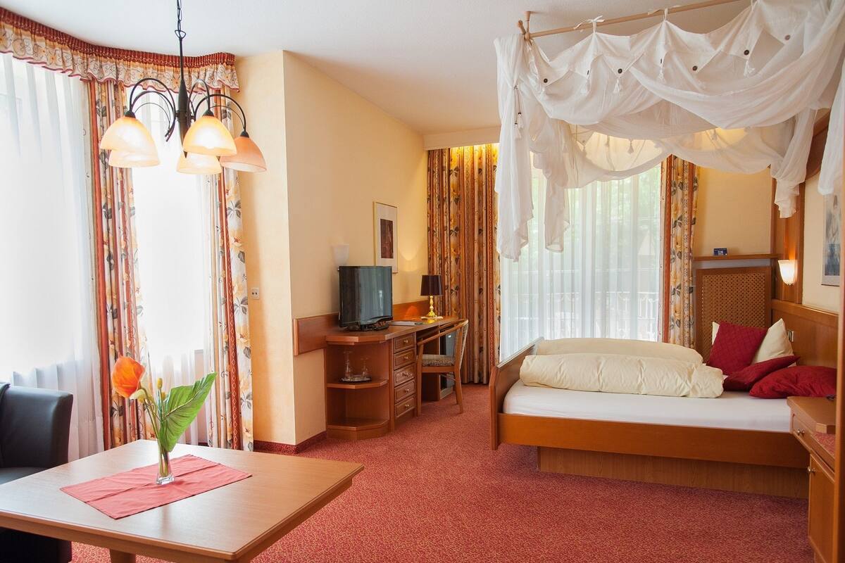 A hotel room with a bed, a desk, a television, and a dining area.