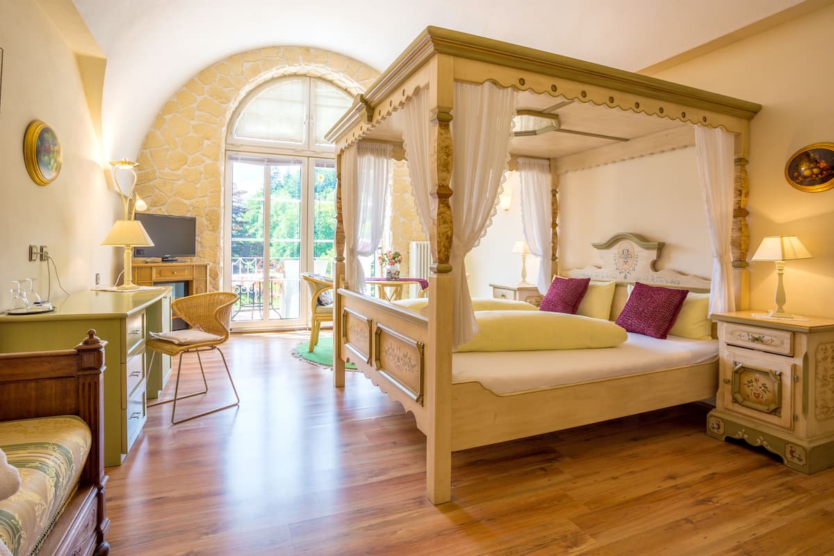 A four-poster bed with a canopy, a television on a stand, a desk with a lamp, and a chair.