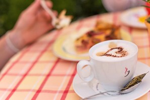 A cup of coffee with a heart-shaped design on the foam, placed on a white saucer with a spoon and a tea leaf beside it. - Parkhotel Bad Faulenbach (Fuessen)