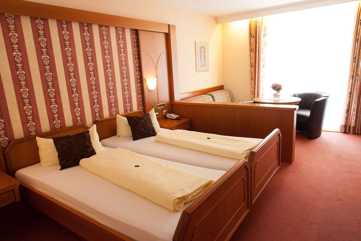 A hotel room with two beds, a desk, a chair, and a window with curtains.