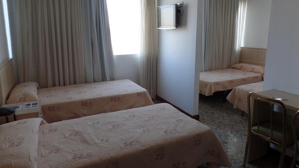 Une chambre d’hôtel avec deux lits simples, un bureau, une chaise et un téléviseur fixé au mur.