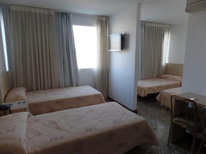 A hotel room with two single beds, a desk, a chair, and a TV mounted on the wall.