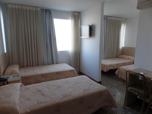 A hotel room with two single beds, a desk, a chair, and a TV mounted on the wall.