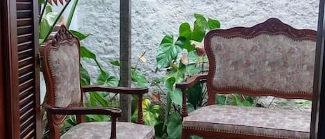 Um deck de madeira com duas cadeiras estofadas e um banco, cercado por vegetação.