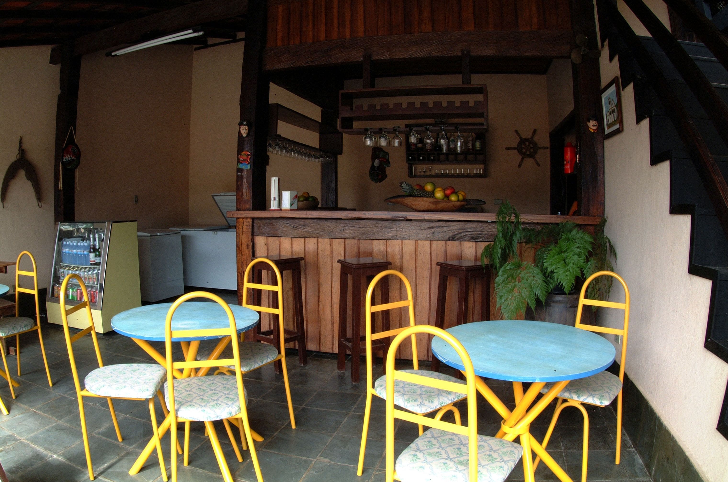 A bar area with wooden tables and yellow chairs, a fruit bowl on the counter, and a potted plant.
