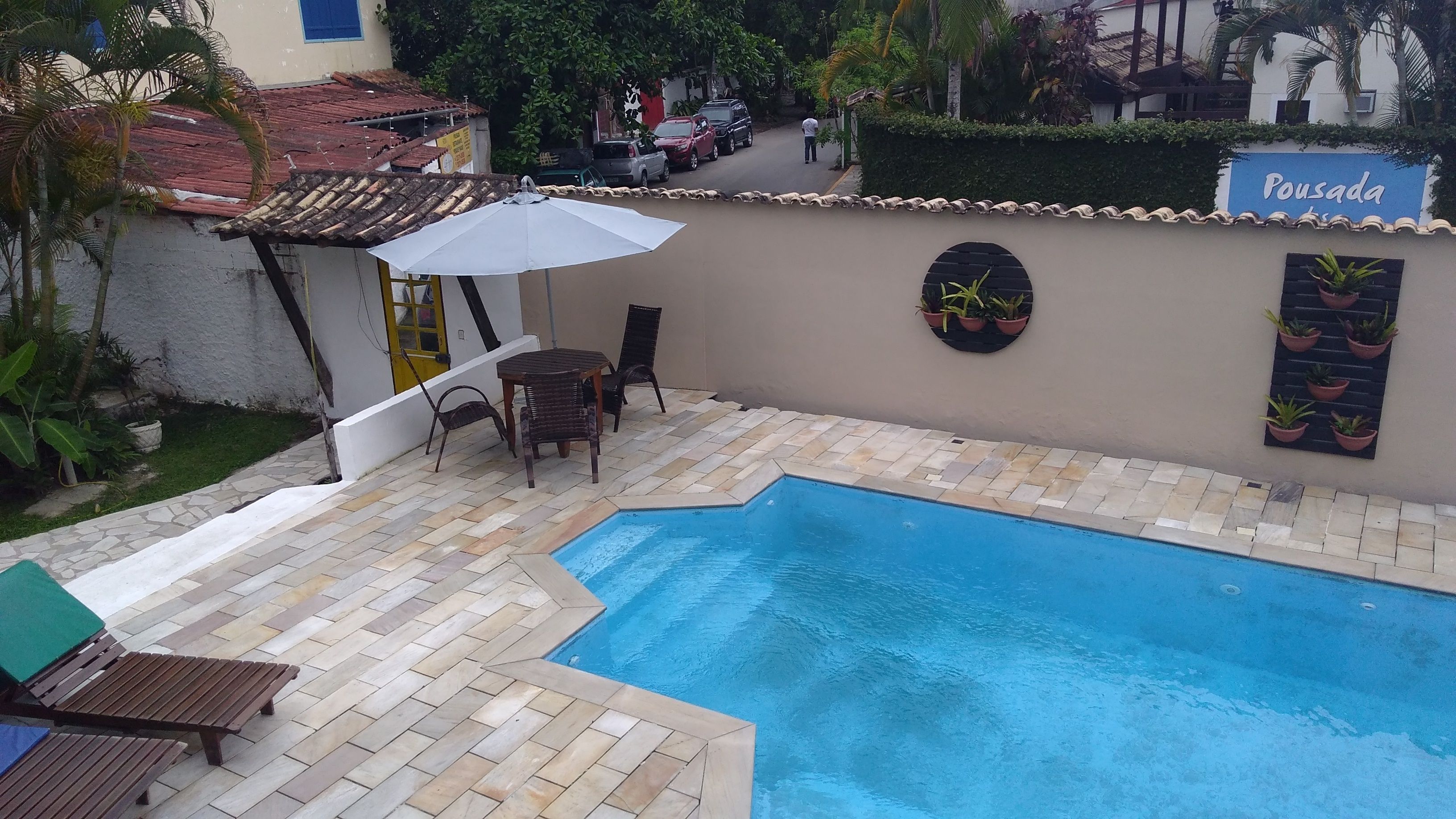 A swimming pool with a tiled deck, a table with chairs, and a sign that reads "Pousada".
