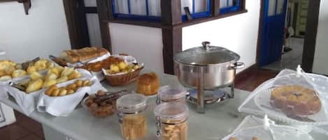 A buffet table with various food items including pastries, bread, and a covered pot, likely containing soup or stew.