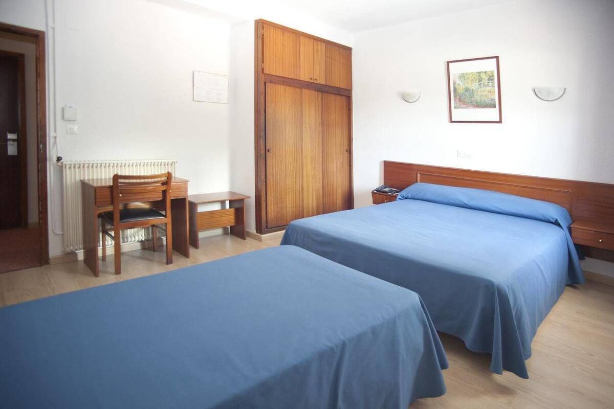 A room with two beds, a wooden desk, and a chair.
