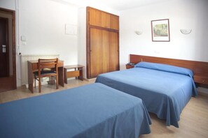 A room with two beds, a wooden desk, and a chair.