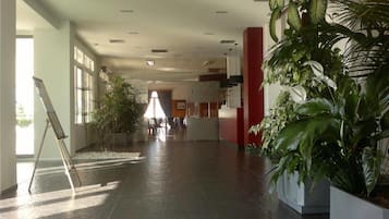 Un vestíbulo amplio con una planta grande en maceta, una recepción y vistas al interior.