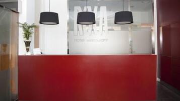 A hotel reception desk with a red counter and three black pendant lights.