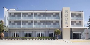 A multi-story hotel with balconies, a central entrance, and a name sign.