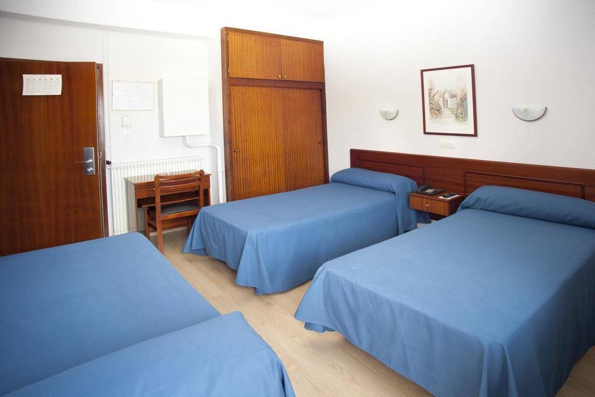 A room with three single beds, a wooden wardrobe, a desk, and a chair.