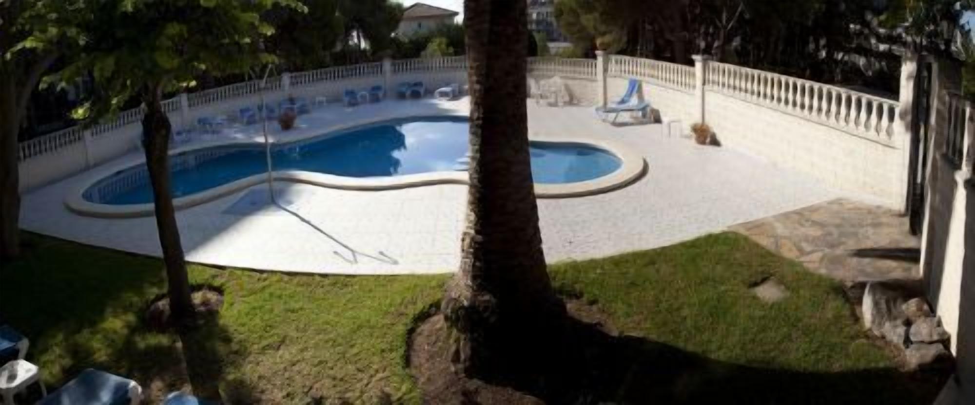 Una piscina con bordo curvo, circondata da un recinto bianco e da un'area verde.