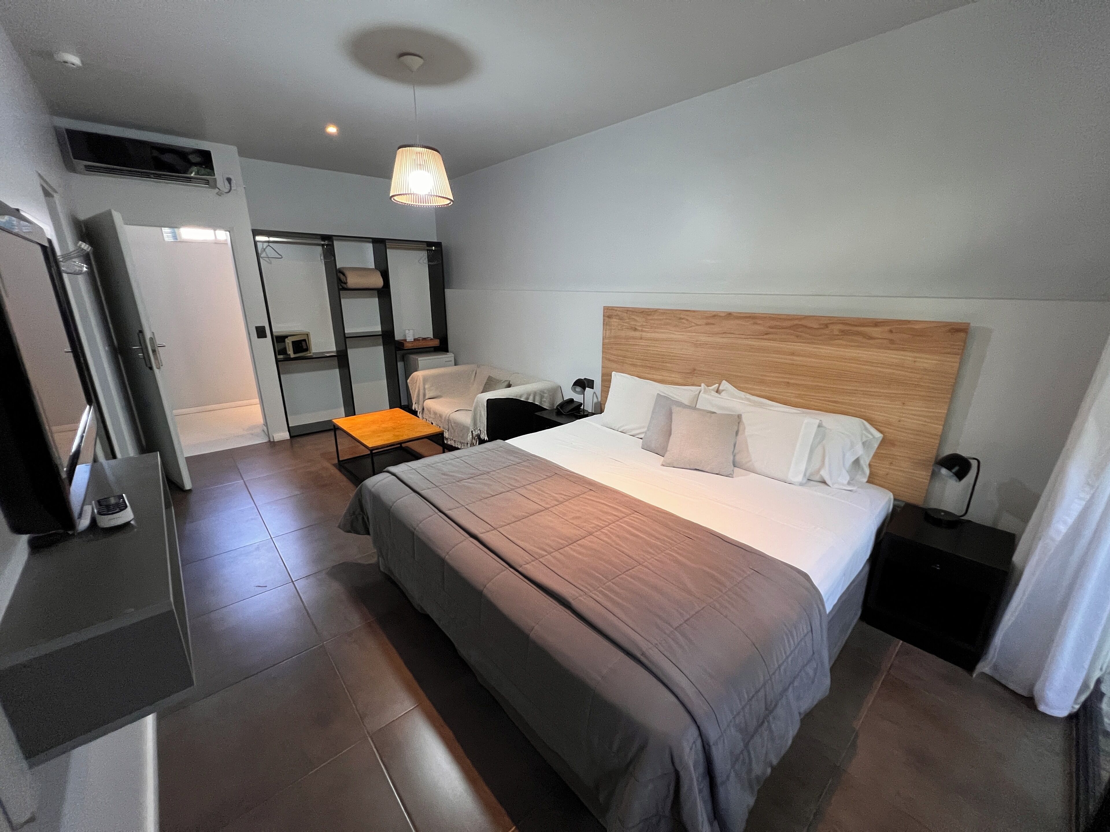 Et moderne hotelværelse med en stor seng, et træhovedgærde, et sengebord, en lampe, et skrivebord med stol og et klædeskab.