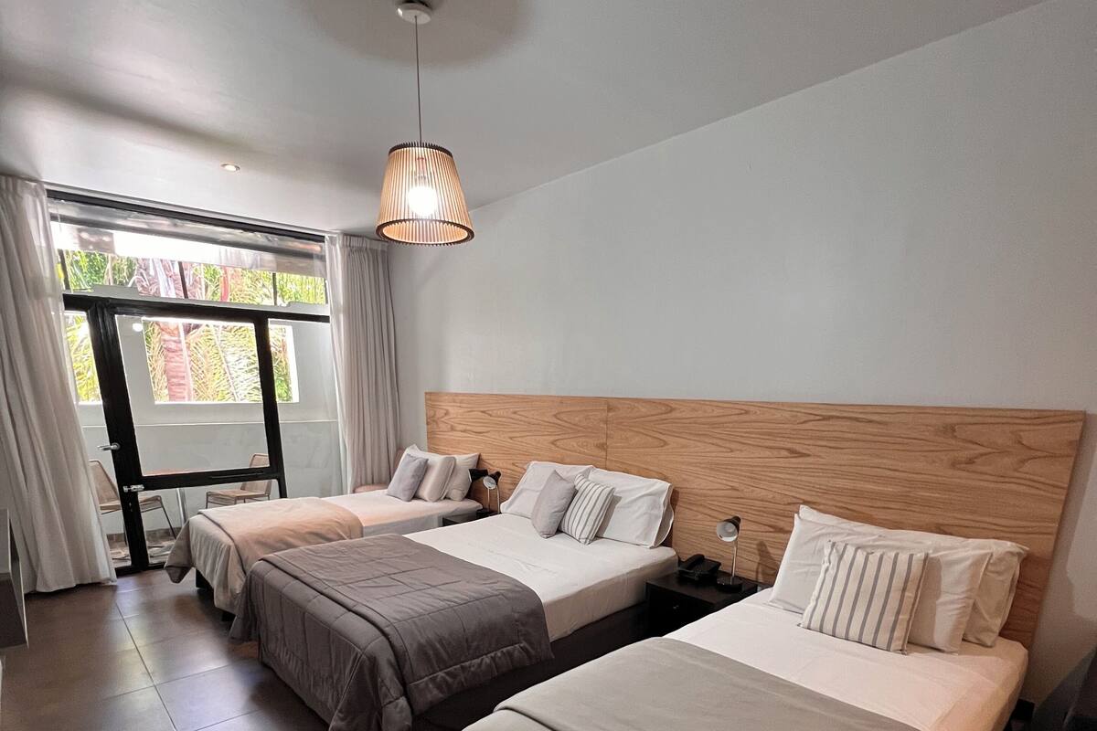 A hotel room with two beds, a wooden headboard, a hanging light fixture, and a view through a glass door.