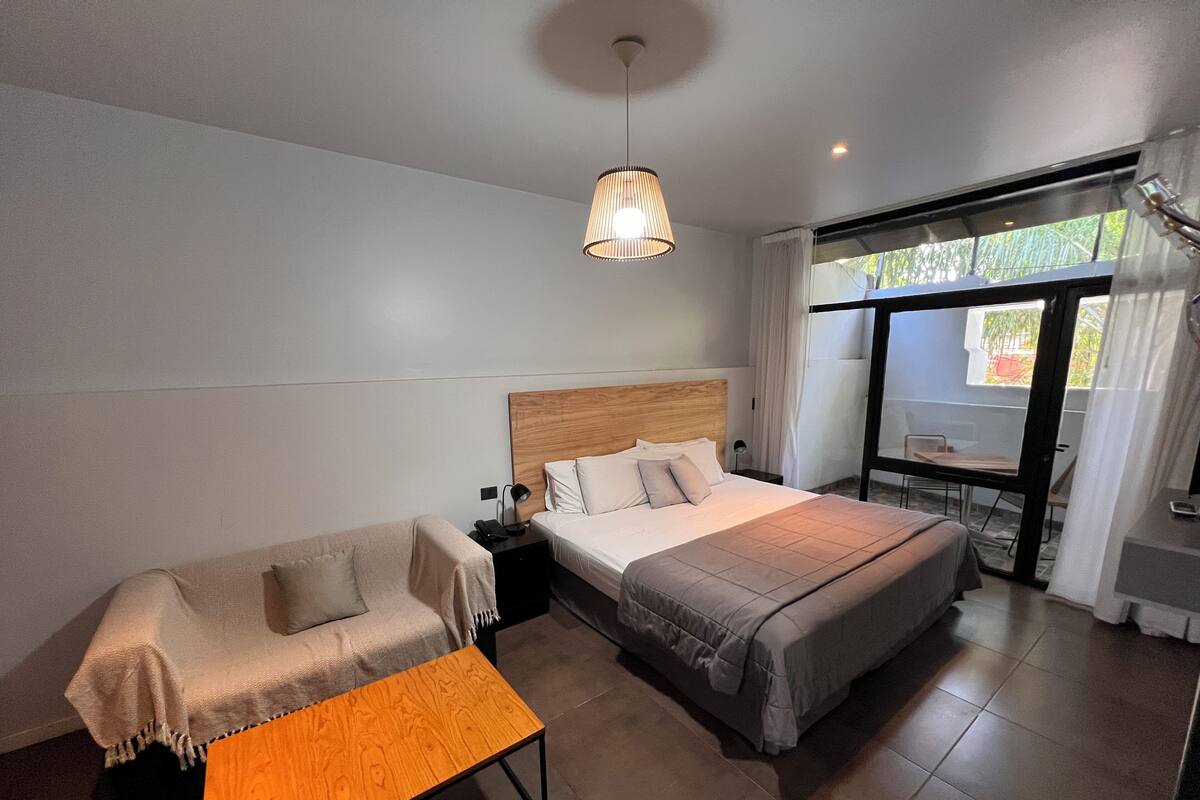 A modern bedroom with a bed, a sofa, a small table, and a balcony with a view.
