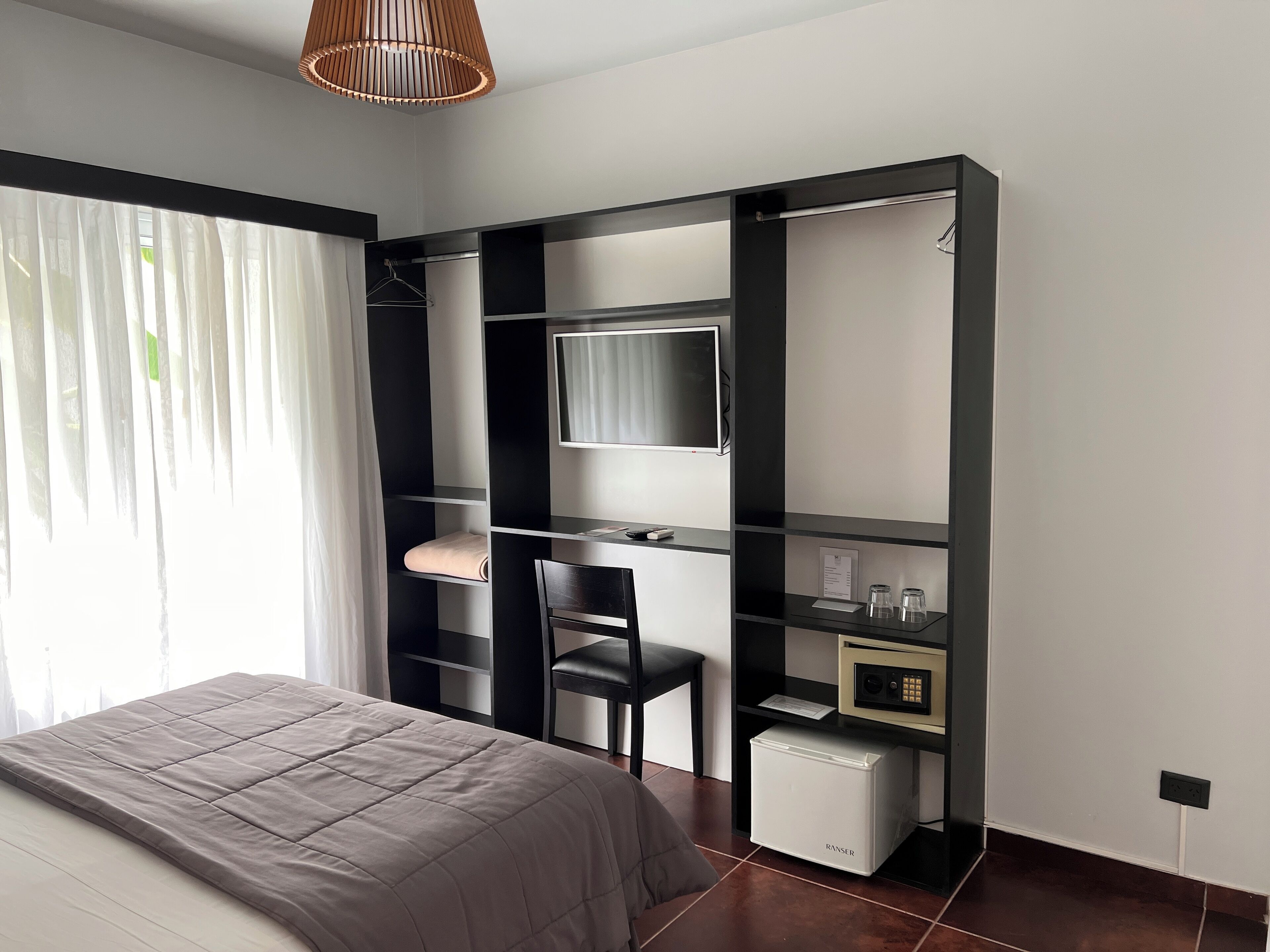 Un dormitorio moderno con cama, escritorio, silla, televisor y un refrigerador pequeño.