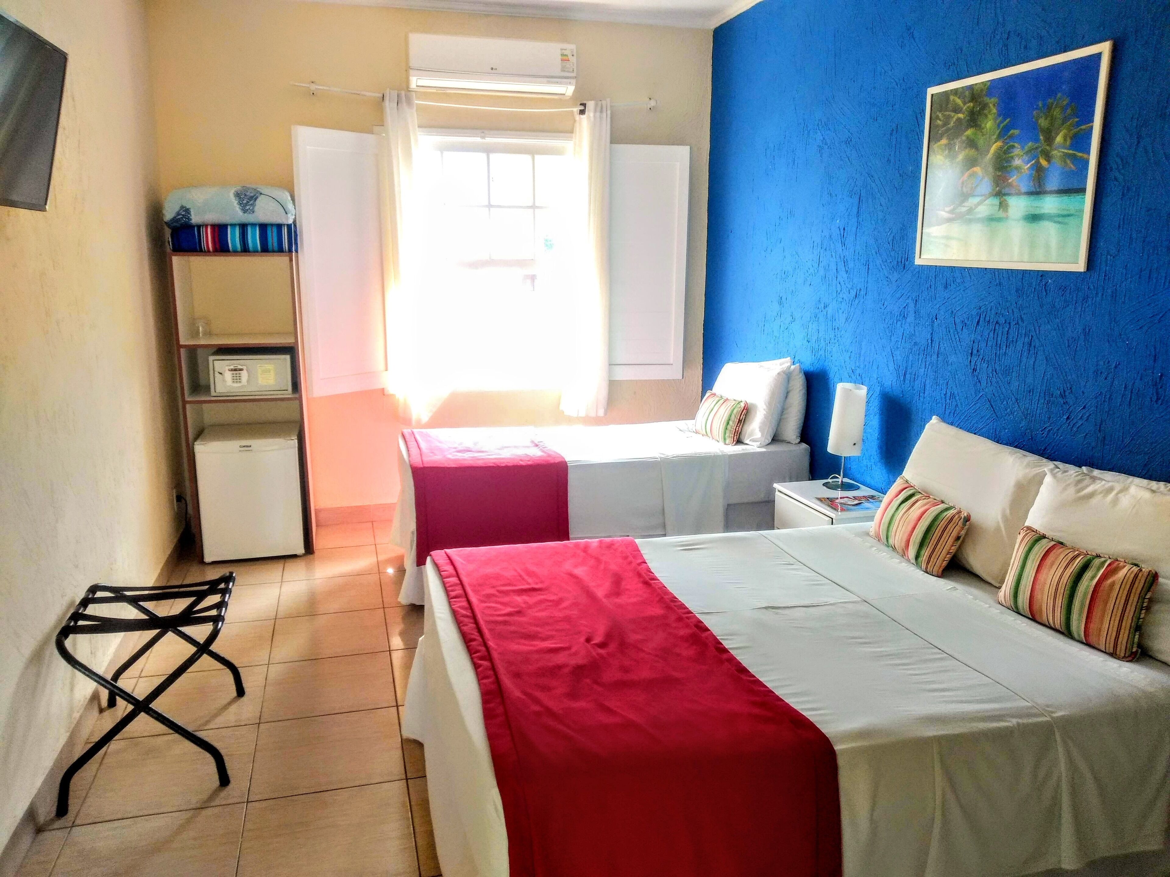 A hotel room with two beds, a desk, a chair, a microwave, and a painting on the wall.
