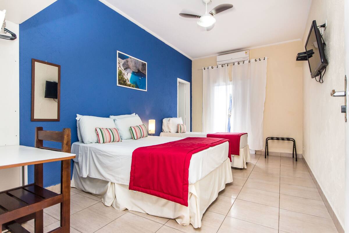 A hotel room with two beds, a TV, a ceiling fan, and a window with curtains.