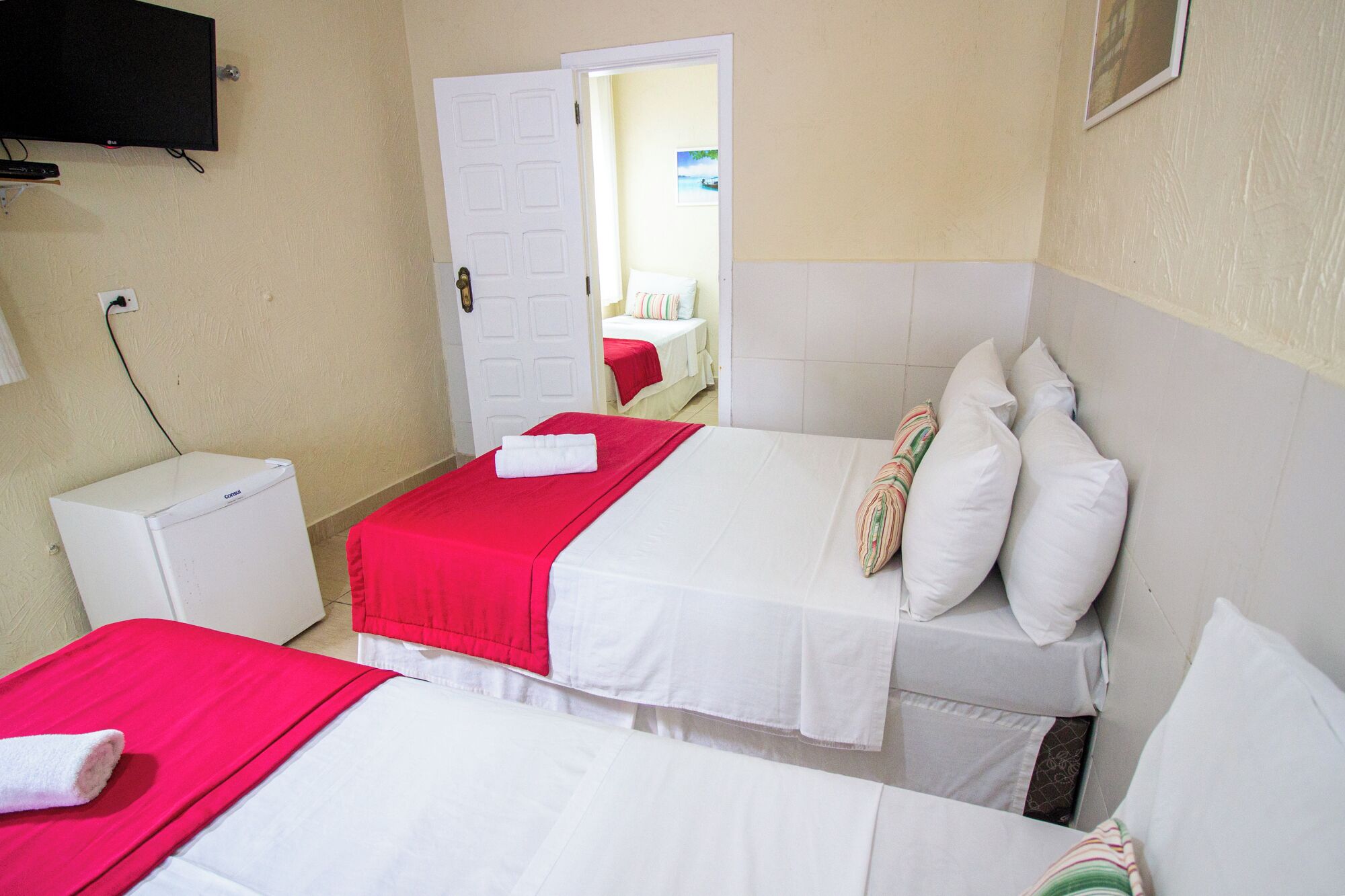 A hotel room with two beds, a TV, a small white cabinet, and a door leading to another room.