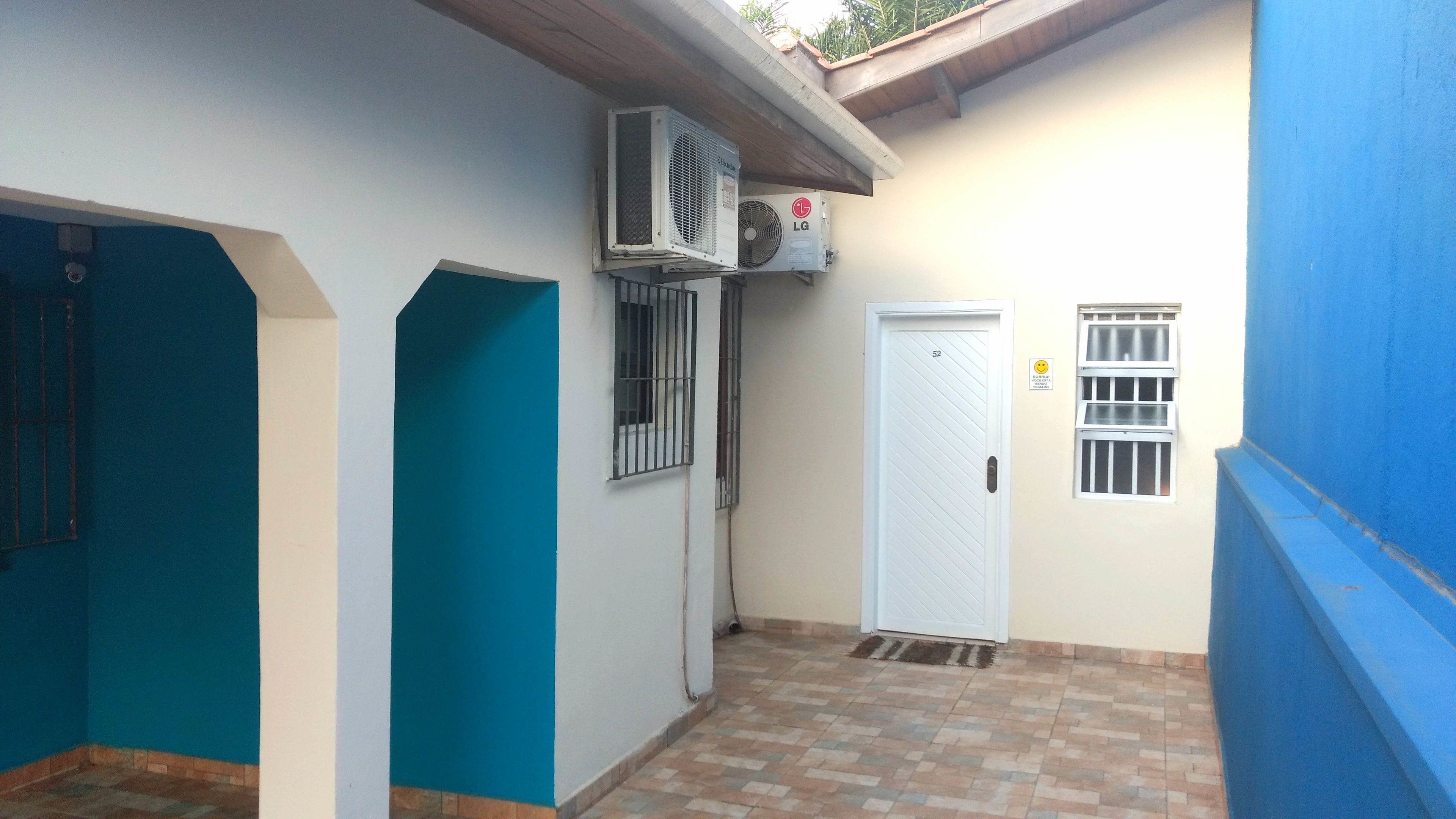 Un pasillo estrecho con suelo de baldosas, una puerta blanca y un equipo de aire acondicionado en la pared.
