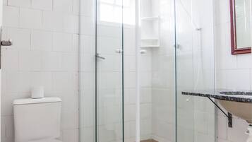 Ein modernes Badezimmer mit einer gläsernen Duschkabine, weißen Fliesen, einer Toilette und einem Waschbecken mit Marmorplatte.